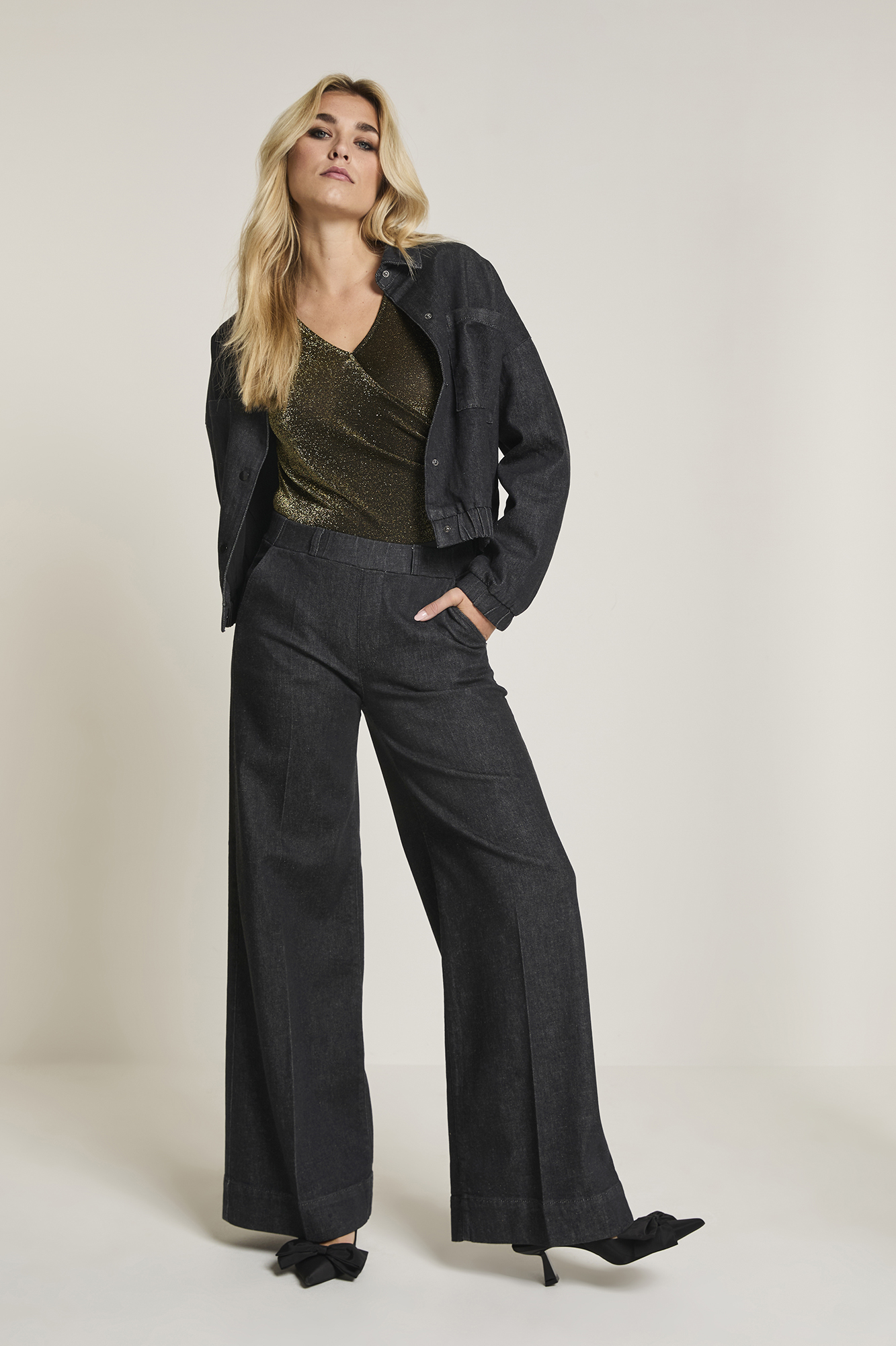 Model draagt Para Mi Lizzy Daily Denims Deep Black, wide leg jeans met hoge taille, gecombineerd met een goudkleurige top en zwarte denim jacket