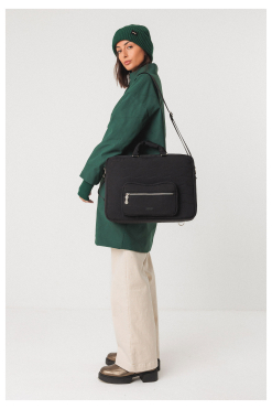Model draagt de zwarte SKFK Cistella tas, draagbaar als crossbody, schoudertas of rugzak, gemaakt van 70% gerecycled polyester, duurzaam en fair geproduceerd.